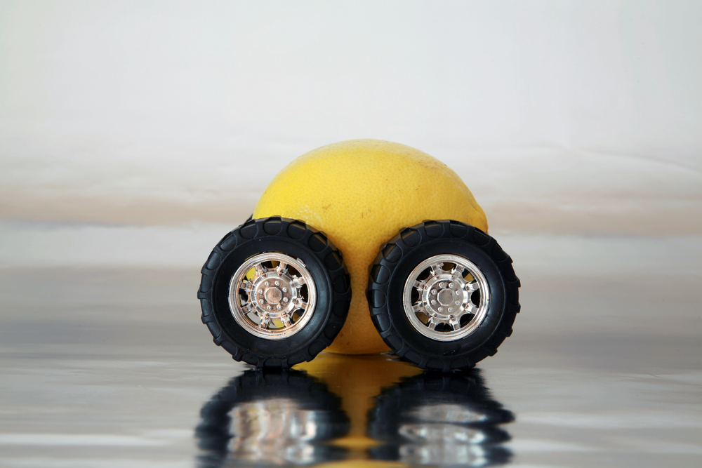 Lemon Law in Florida concept image shows a lemon with two vehicle wheels in front of it to resemble a vehicle